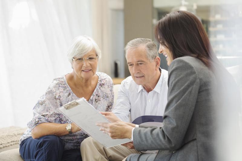 A female hospital staff member discusses information with an elderly couple.