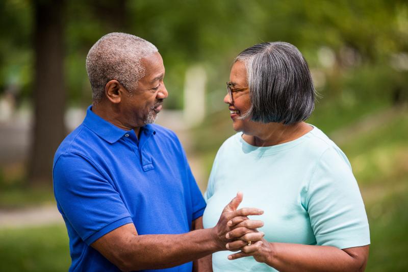 An elderly couple, enjoying each other company while grabbing hands in the park.
