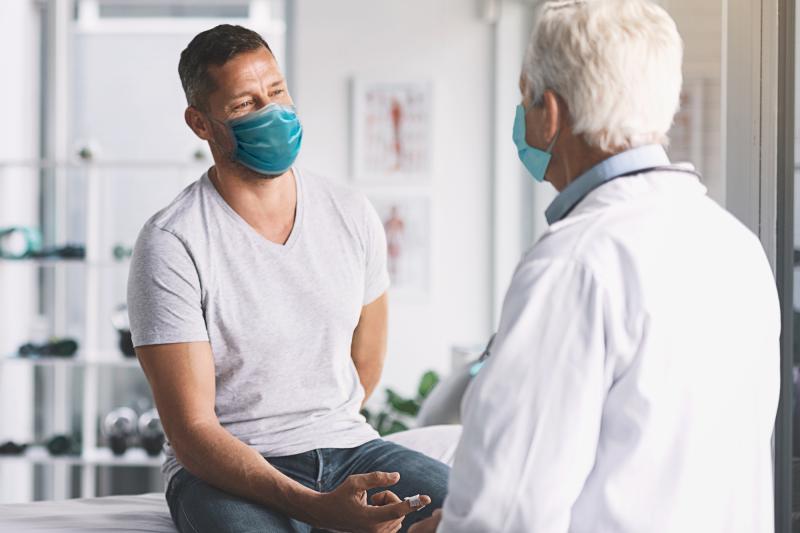 Man talking with doctor while both are wearing masks.