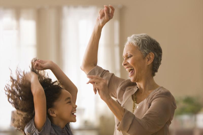 An elementary-aged girl and an older female relative dancing and smiling indoors