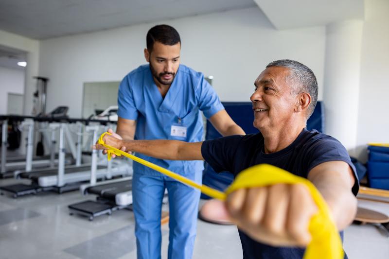 Physical therapist helping a patient with arm band, and stretching out his arms.