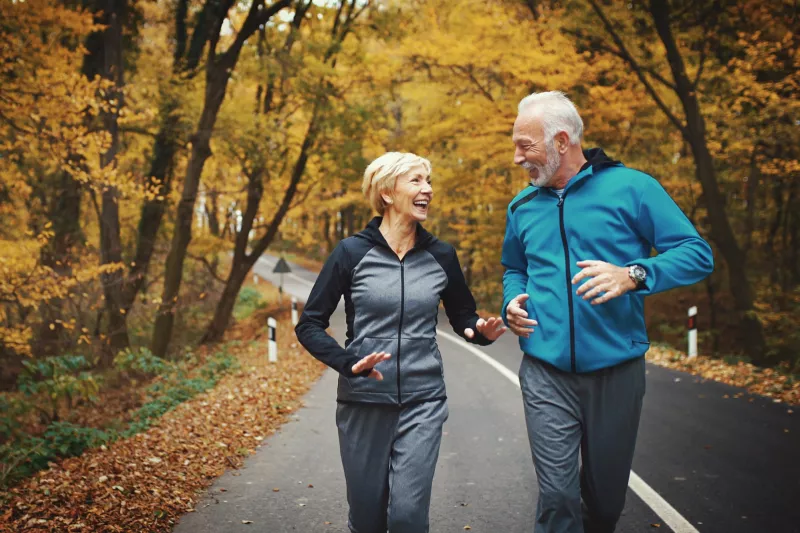 Older couple jogging on a path through the trees