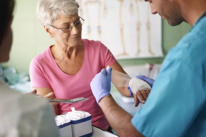 An older woman has her hand bandaged by a nurse