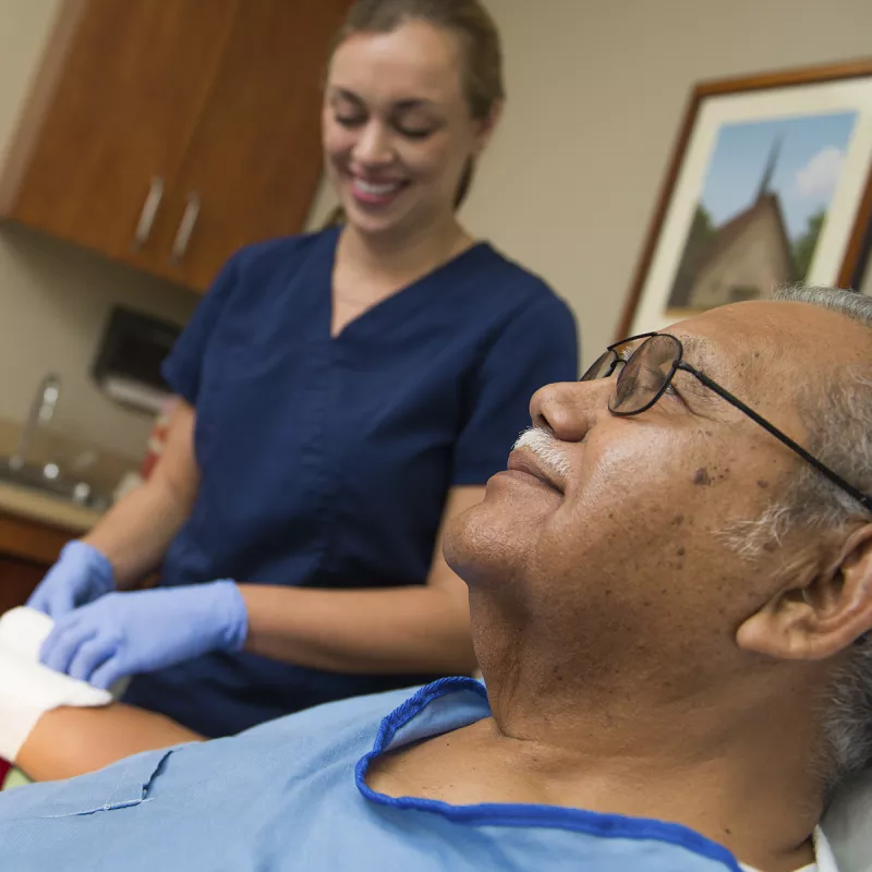 A nurse tends to a Hispanic man's wrist wound.